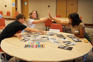 Three youths at a table during youth forum, two of them high five each other.