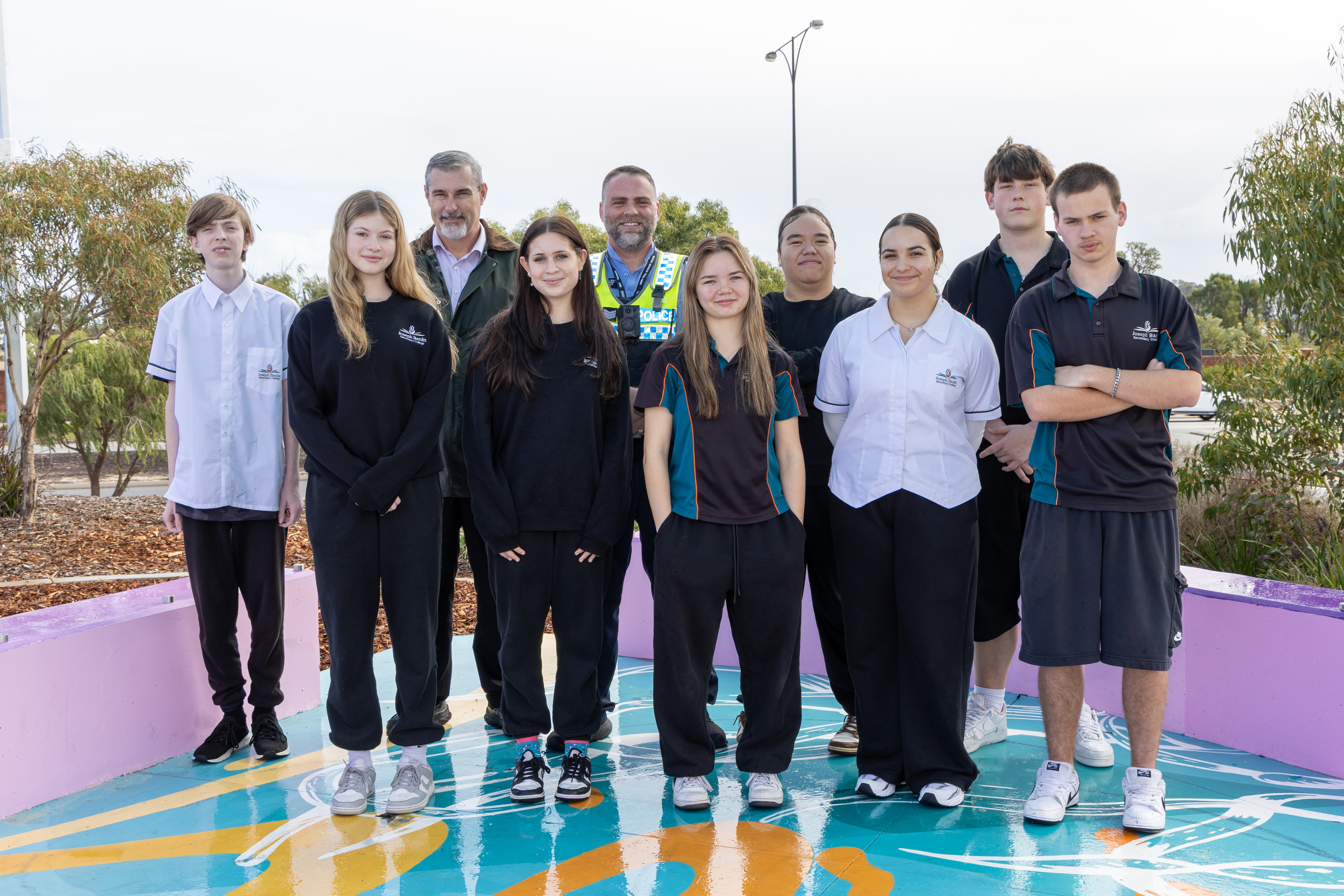 Group of high school students and police officer standing on youth mural.