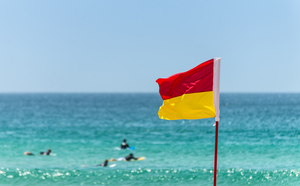 A red and yellow flag on the beach with the ocean in the background.