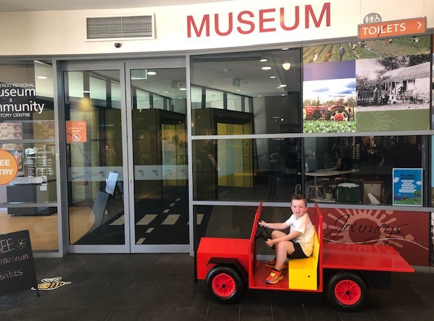 Boy on small red truck in front of museum entrance