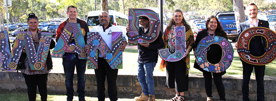 Multicultural group holding 'WANDJOO' signage