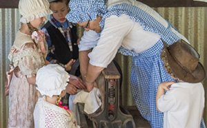 People in old clothes using a mangle to do washing