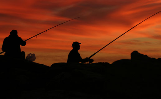 People fishing in front of a sunset
